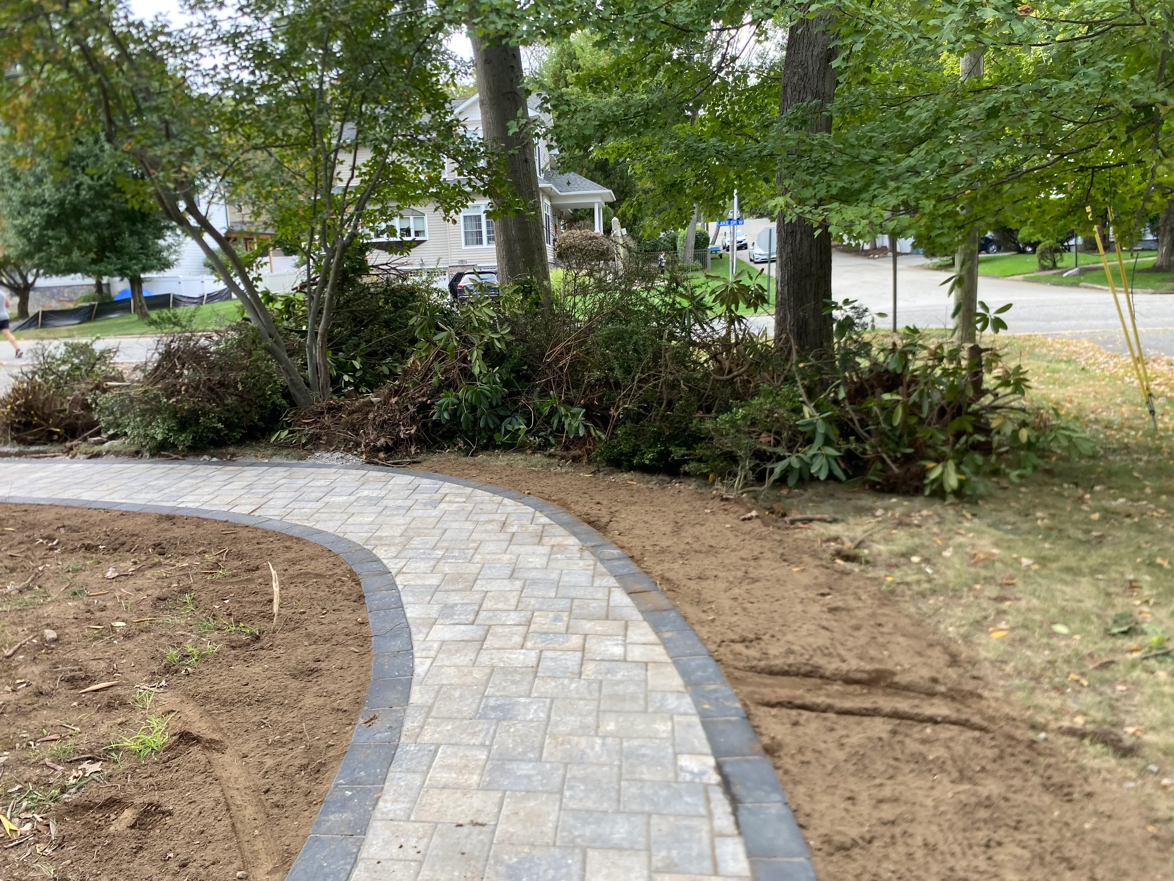 Curved paver walkway with herringbone pattern and dark border edging through residential front yard