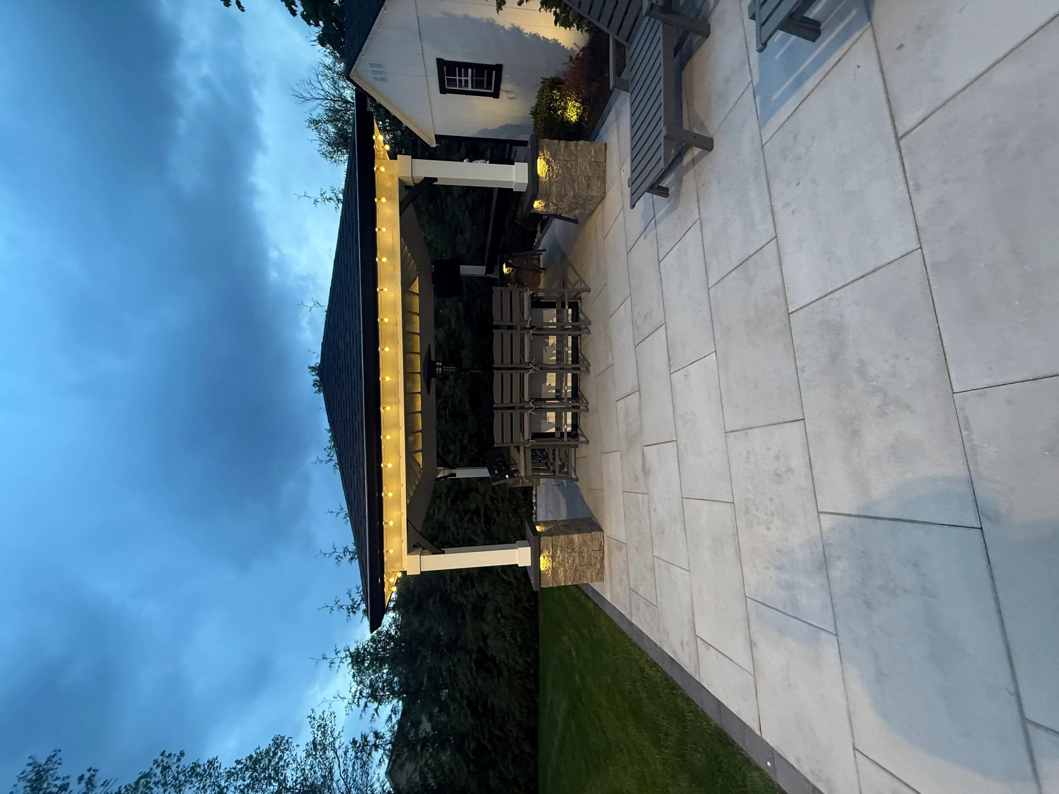 Outdoor kitchen with built-in grill, stone veneer, pavers, and accent lighting at dusk