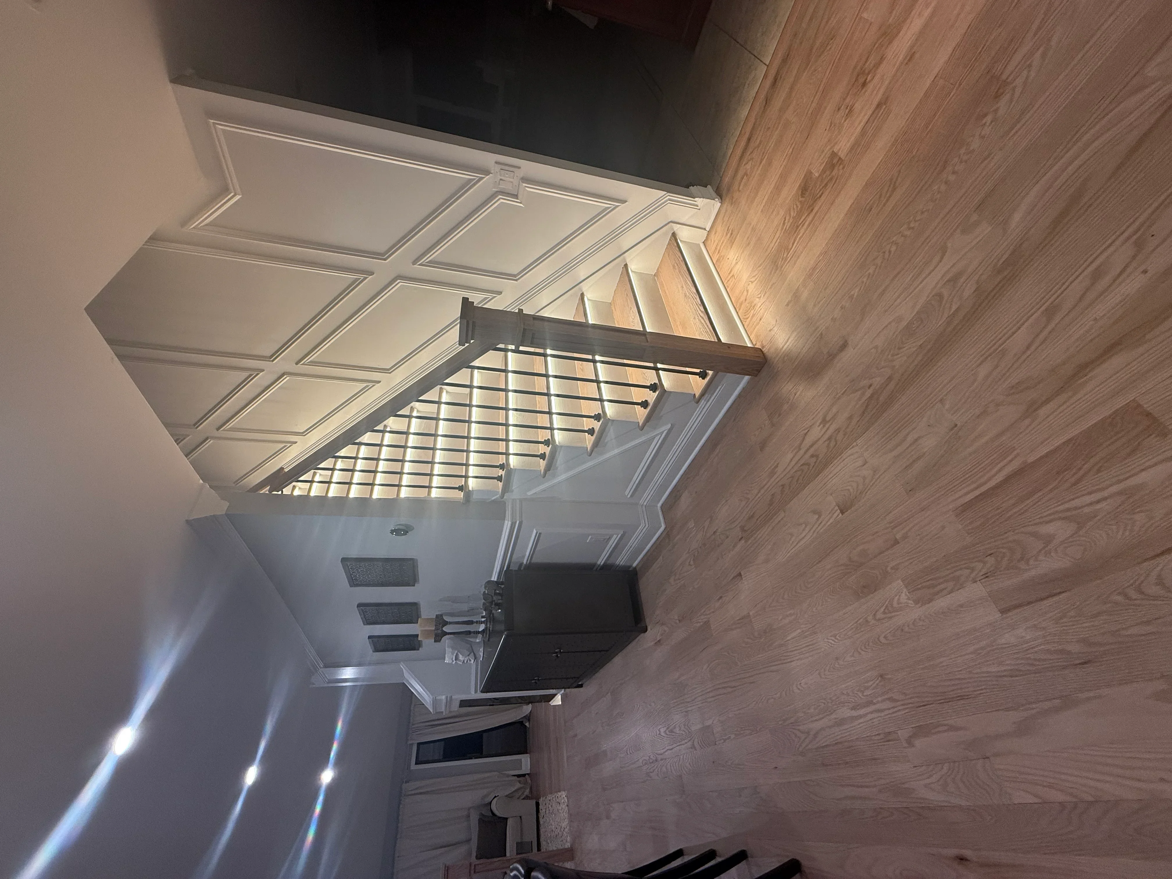 Coffered ceiling with crown molding, white cabinetry, hardwood flooring, and metal stair railing in renovated kitchen