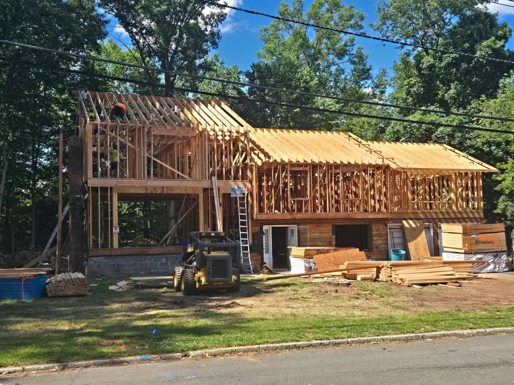 Wood-framed residential addition with exposed studs, roof trusses, and structural sheathing during construction