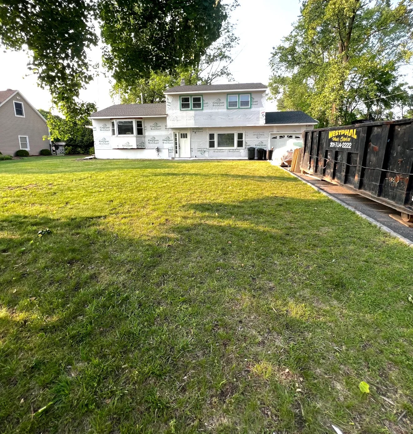 House wrapped in protective sheeting during renovation preparation with dumpster on-site