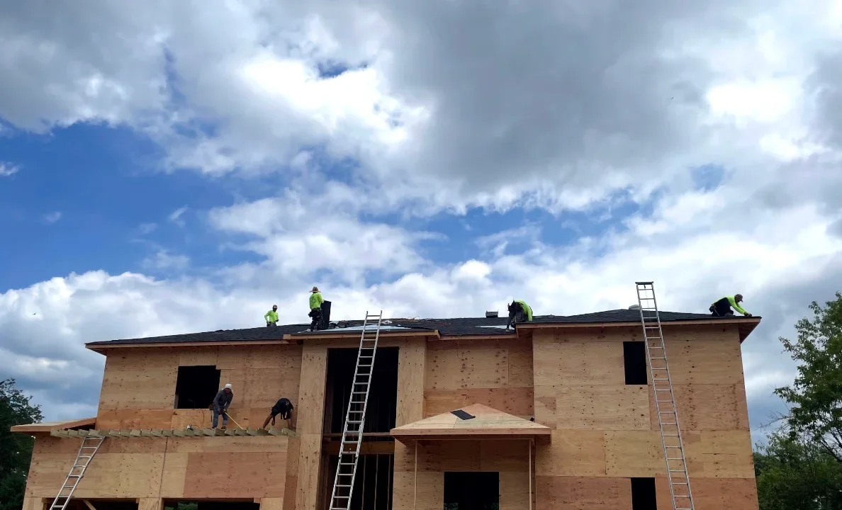 Roofers installing dark asphalt shingles on two-story home with pitched roof
