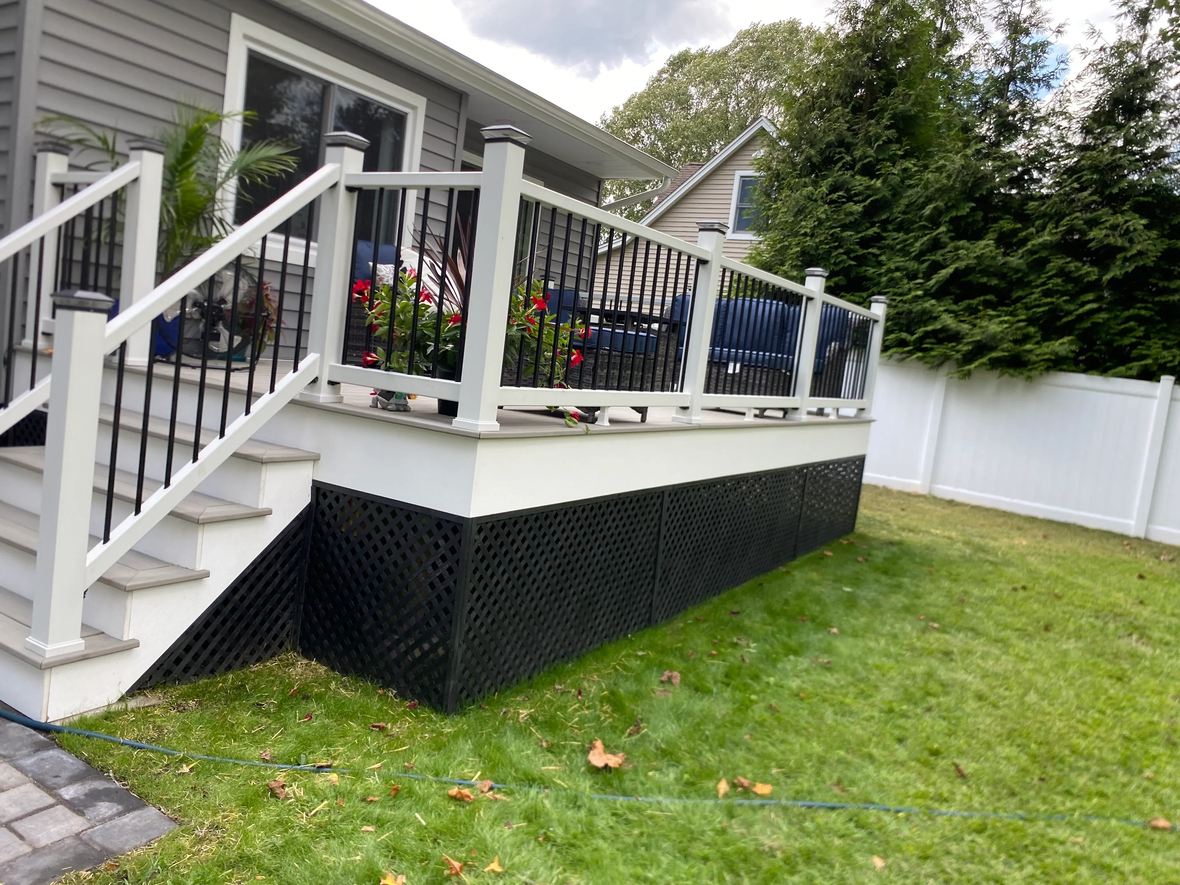White deck with black metal railing, lattice skirting, and concrete steps