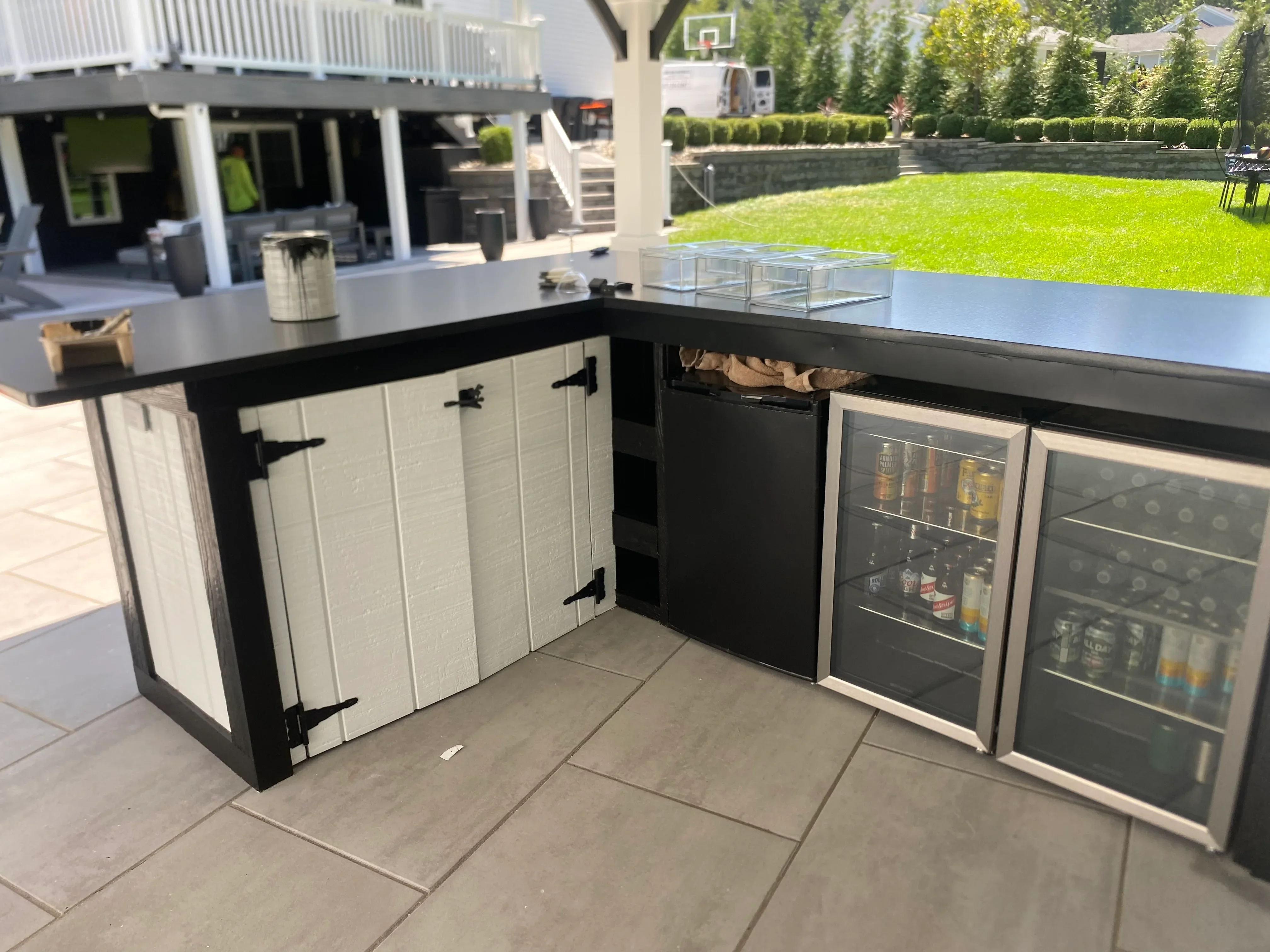 Outdoor kitchen island with white cabinetry, black countertop, and dual beverage coolers on paver patio