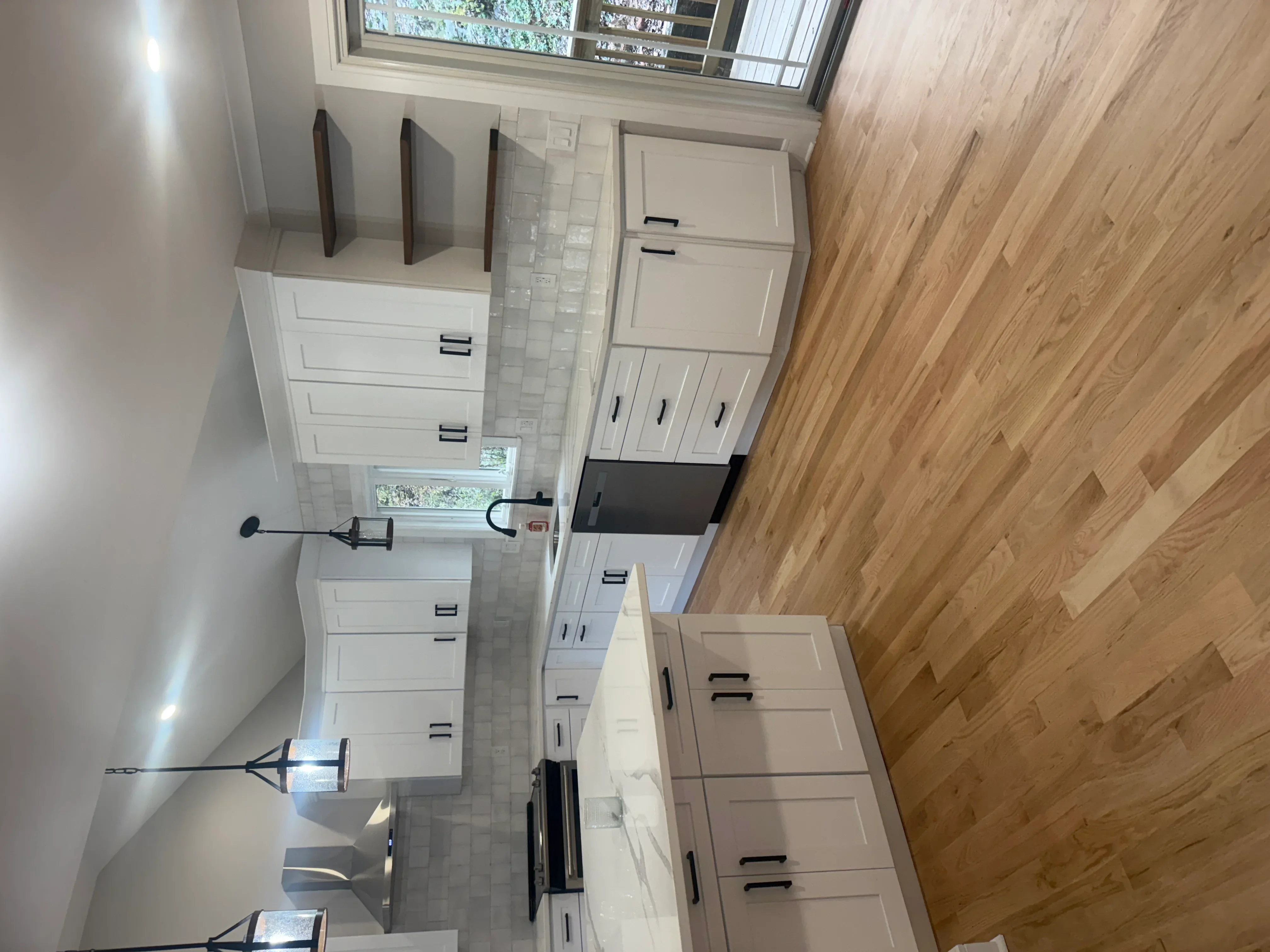 White kitchen cabinets with black handles, subway tile backsplash, stainless steel range, and wood flooring