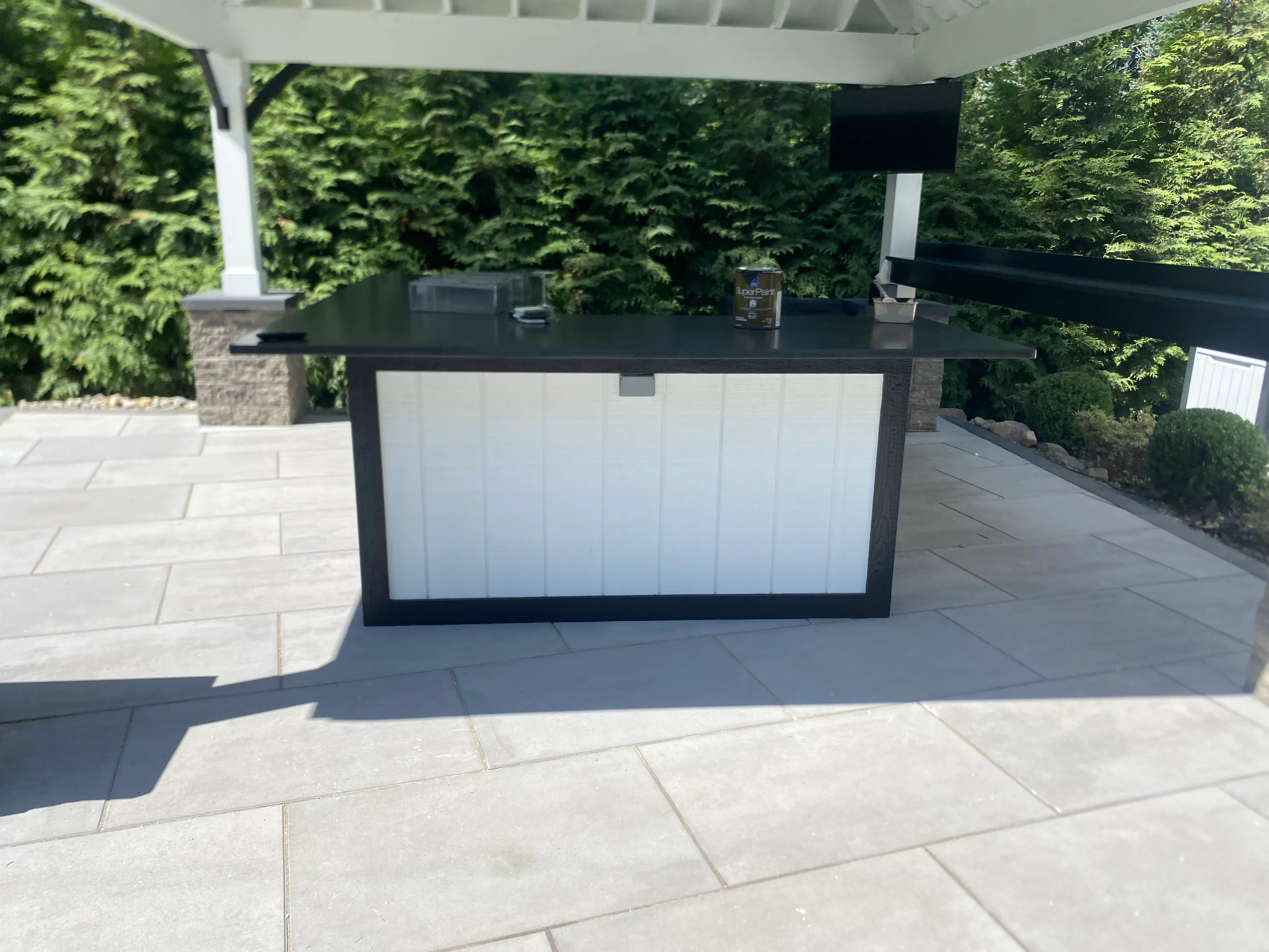 Black metal outdoor kitchen bar with white cabinetry and dark countertop under white pergola