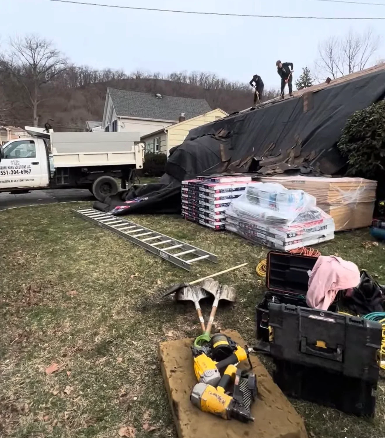 Roof replacement in progress with old shingles removed, new materials staged, and workers installing roofing