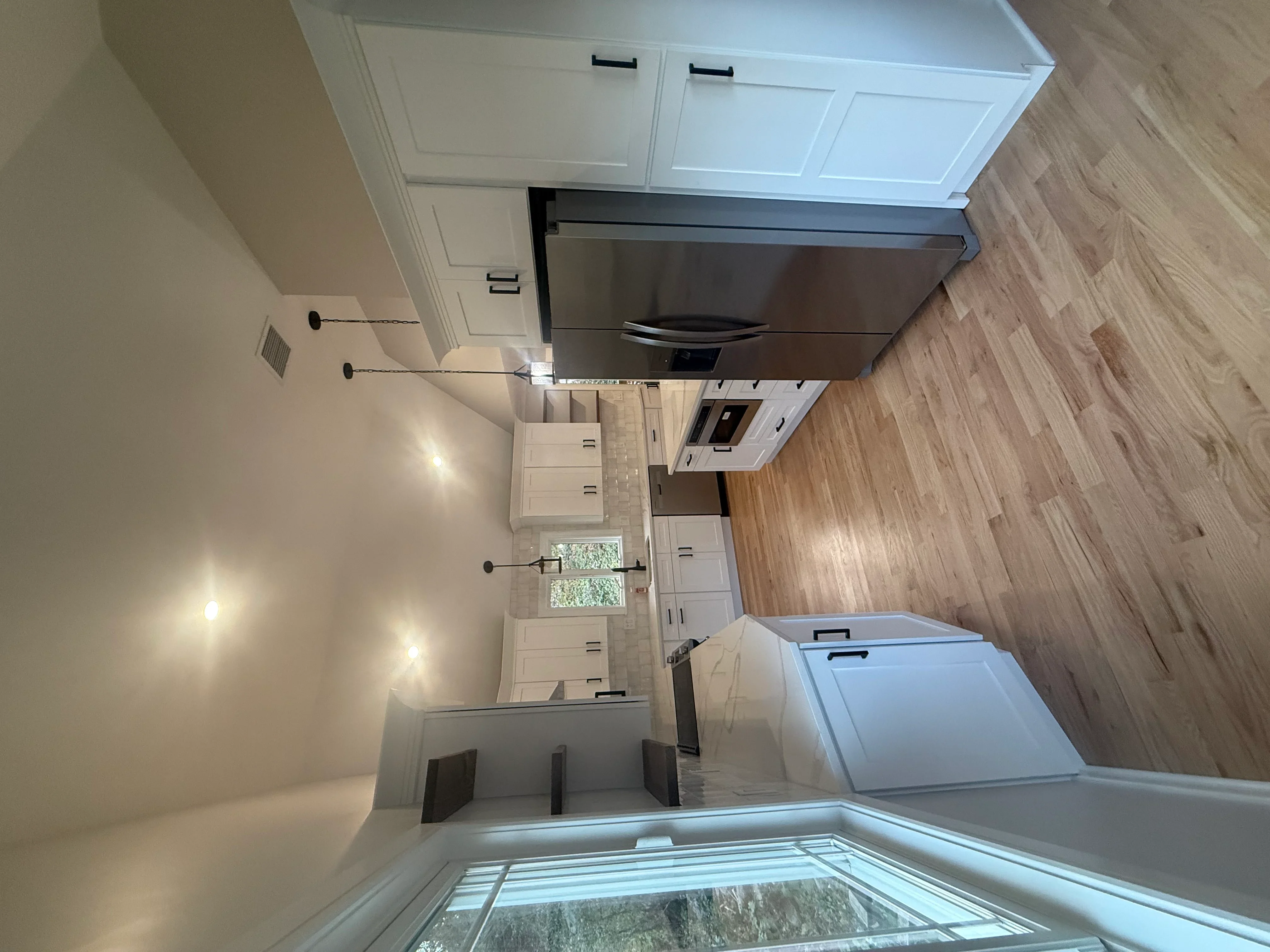 White kitchen cabinets, stainless steel appliances, engineered wood flooring, recessed lighting