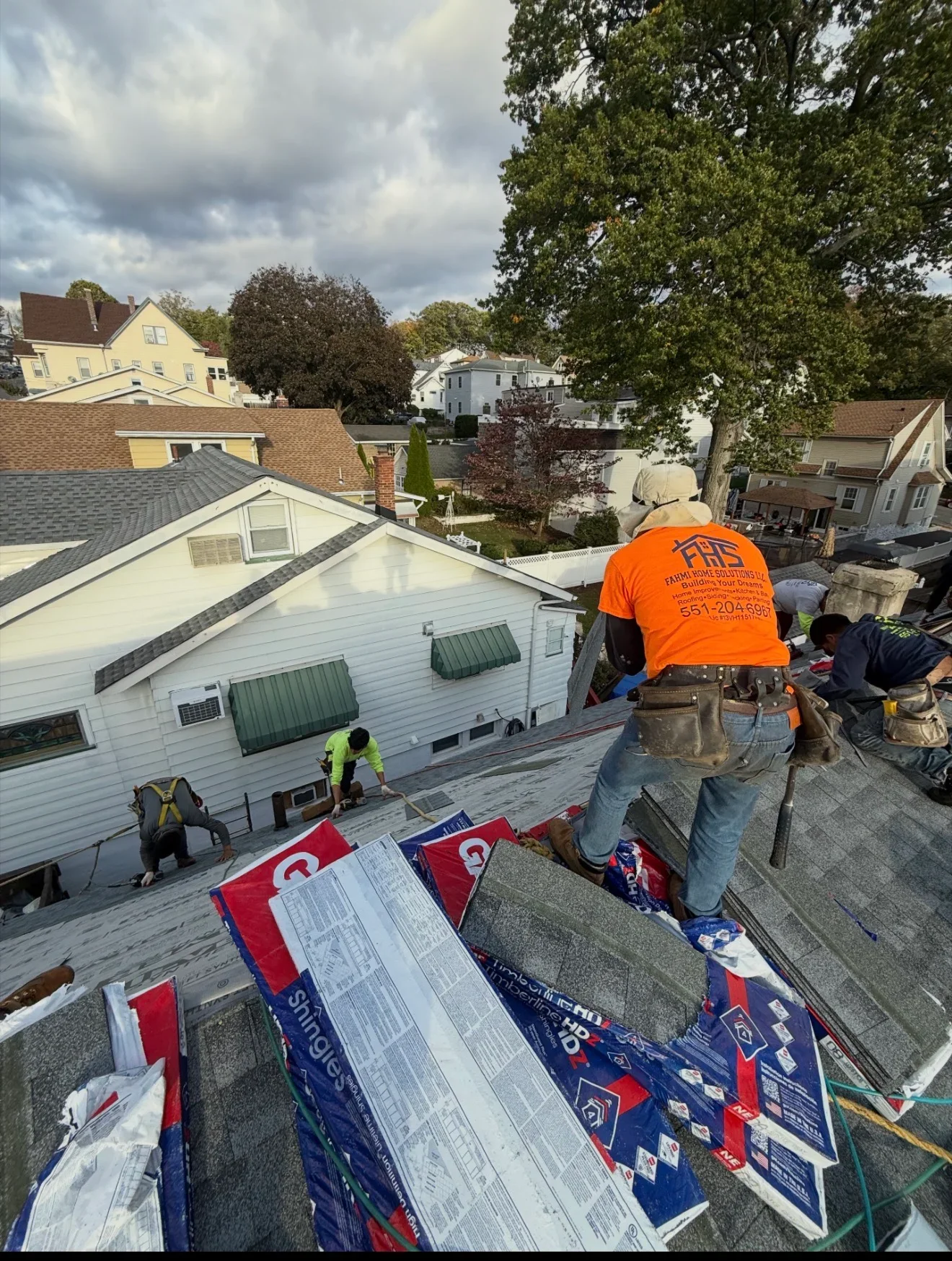 Roofers installing gray asphalt shingles on residential home roof with white siding