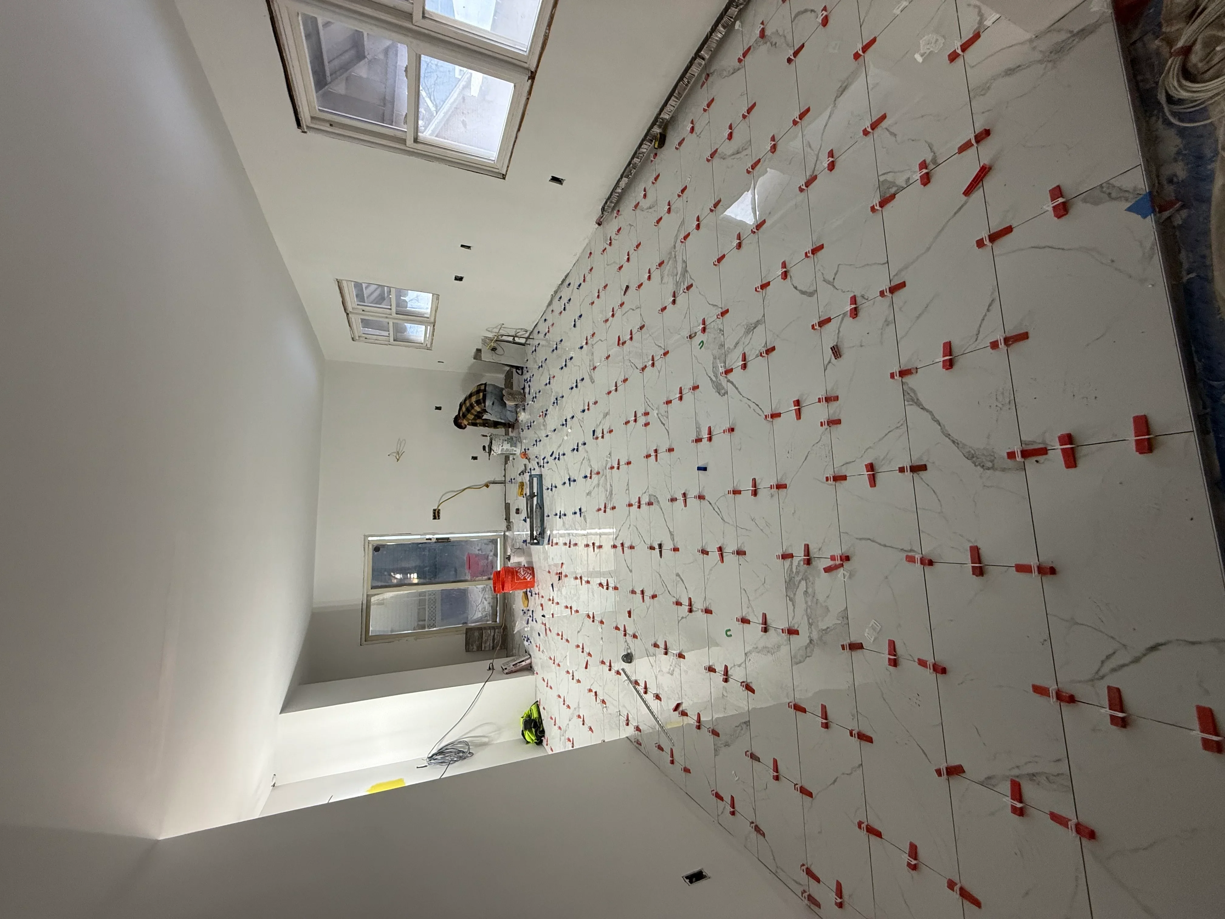 Marble-look ceramic tiles with red spacers on kitchen wall during installation