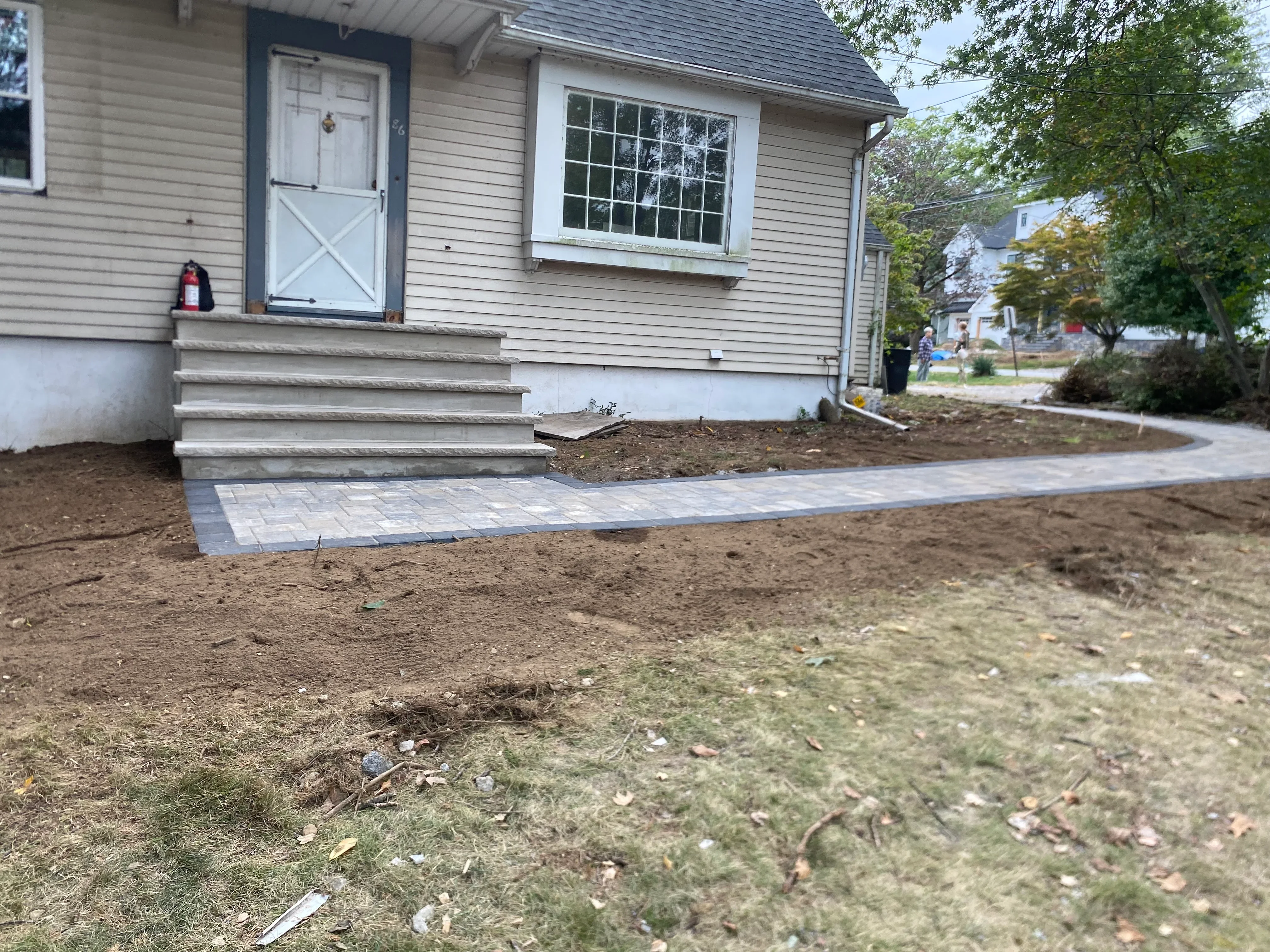 Gray concrete paver walkway installed at residential front entry with prepared soil landscaping