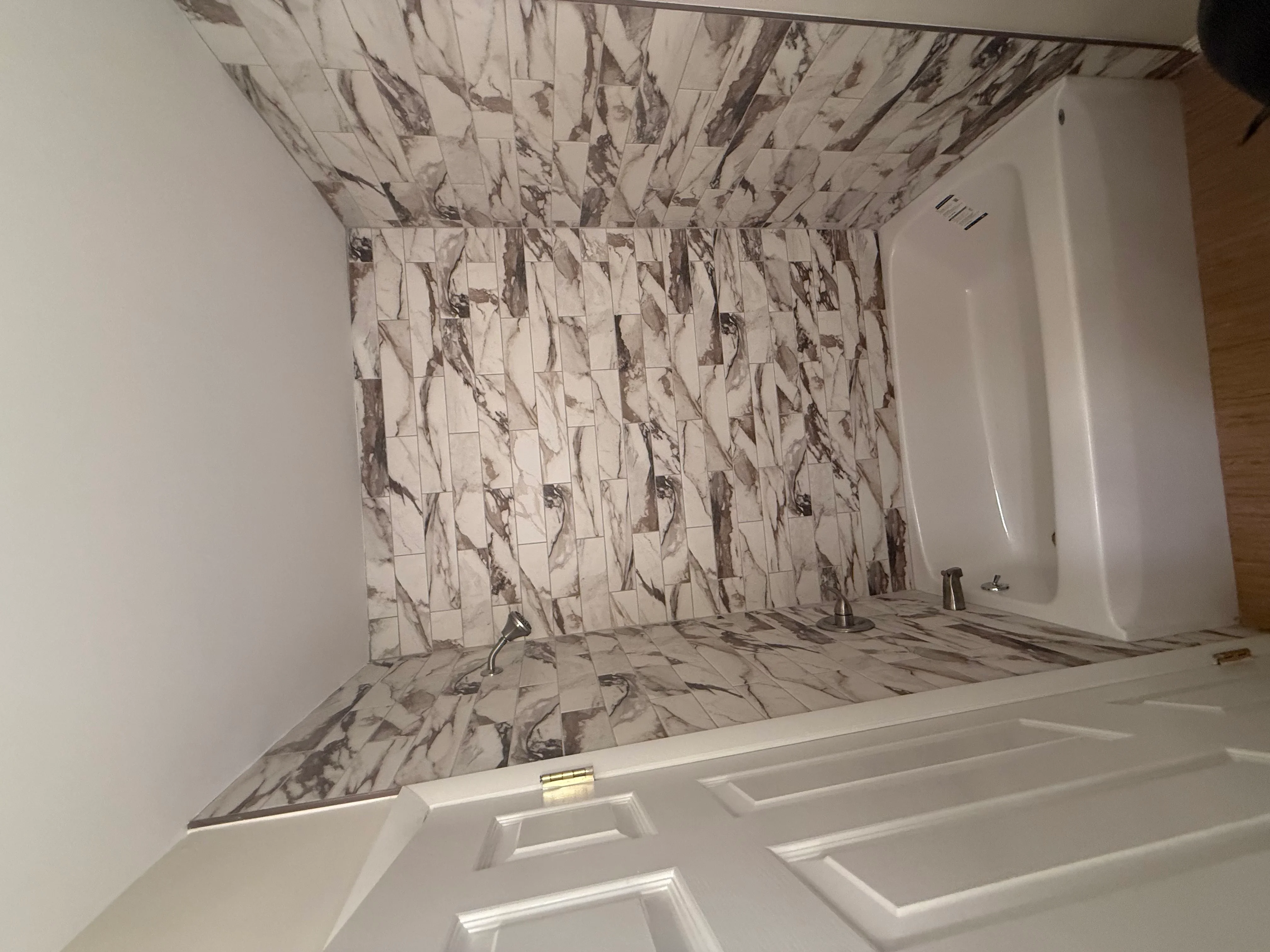 Marble tile shower surround with gray veining in staggered brick pattern on walls and ceiling